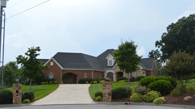 A large brick house with driveway and landscaped yard. Photo