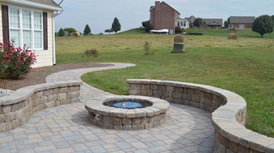 A paved patio with curved walls, fire pit, and walkway. Photo