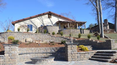 A backyard with stone walls, steps, fire pit, and house. Photo