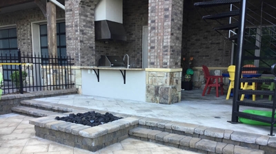 A covered patio with a fire pit, grill, and outdoor kitchen. Photo