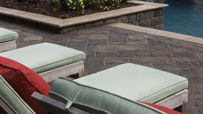 Patio with lounge chairs, cushions, and a stone pool edge. Photo