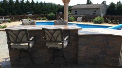 Outdoor bar with chairs next to a pool, stone counter, and walls. Photo