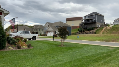 A suburban street with houses, a white truck, and neatly trimmed lawns. Photo