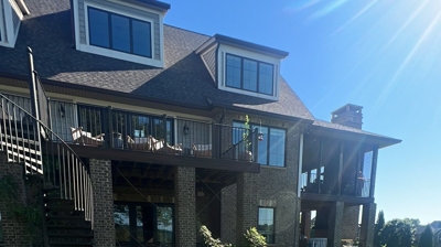 A large house with a deck and stairs, set back from a grassy hill. Photo