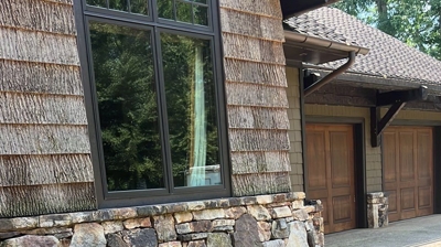 A house with a stone foundation, low plants, and dark brown mulch, leading to a light-colored driveway. Photo