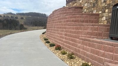 A curved reddish-brown stone wall runs alongside a driveway. Photo
