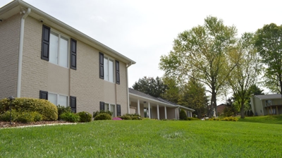 A light beige house sits on a lawn with green trees. Photo