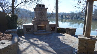 An outdoor patio with a stone fireplace and a view of a lake. Photo