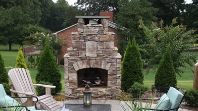 A patio with a stone fireplace and chairs. Photo