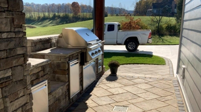 Outdoor kitchen with grill, cabinets, and paved patio. Photo