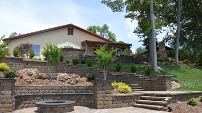 Stone walls, stone steps, plants in mulch, grass and a small stone fire pit in the backyard. Photo