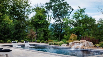 Large swimming pool with a stone waterfall, fire pit and patio furniture Photo