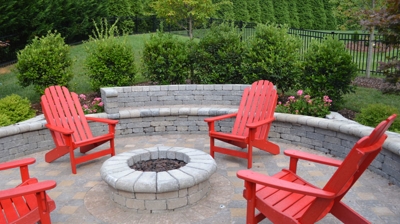Circular patio with fire pit and red Adirondack chairs and stone walls Photo