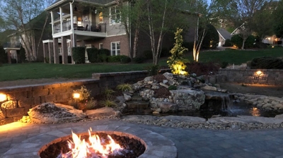 stone fire pit in front of a waterfall into a small pond Photo