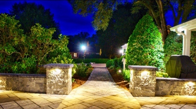 Patio area with 2 stone columns leading to a yard surrounded with trees and plants. Photo