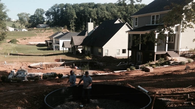 2 men working on a dark gray pool liner and gravel base behind a house Photo